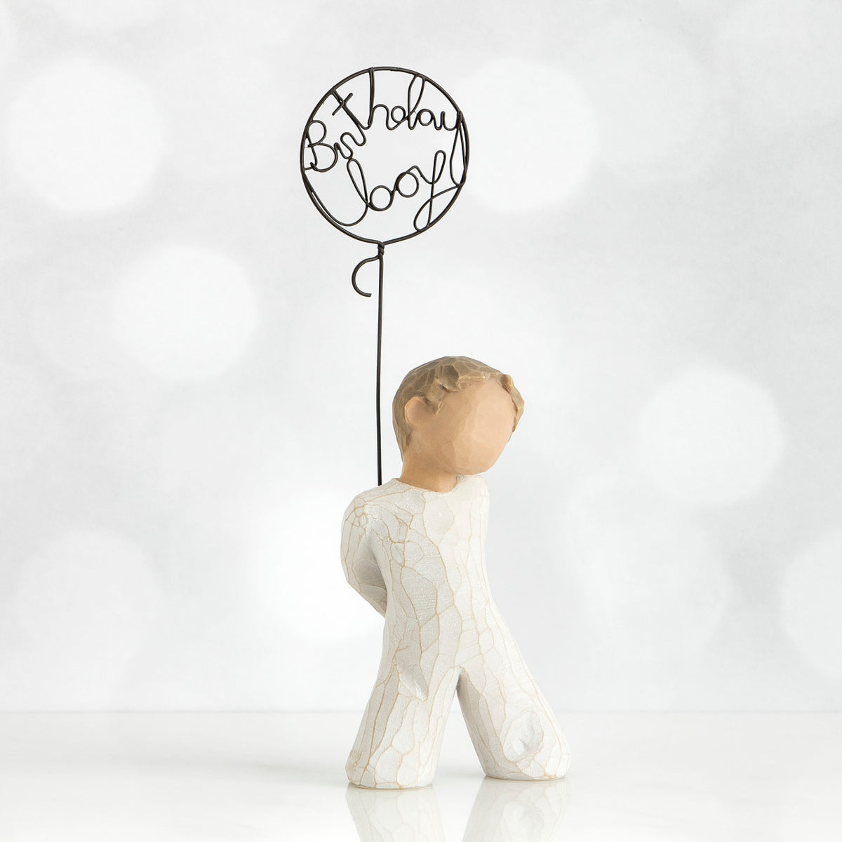 Front view of little boy with light brown hair holding a wire balloon behind his back. Text on balloon is wire