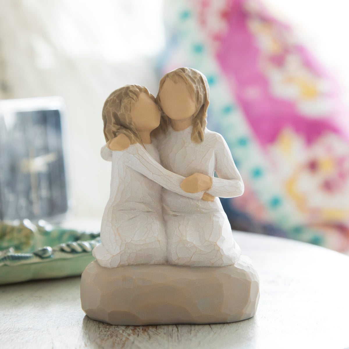 Willow Tree Sister mine, 4”h hand-painted resin figure of two girls in cream dresses, kneeling with arms around each other, on beside table