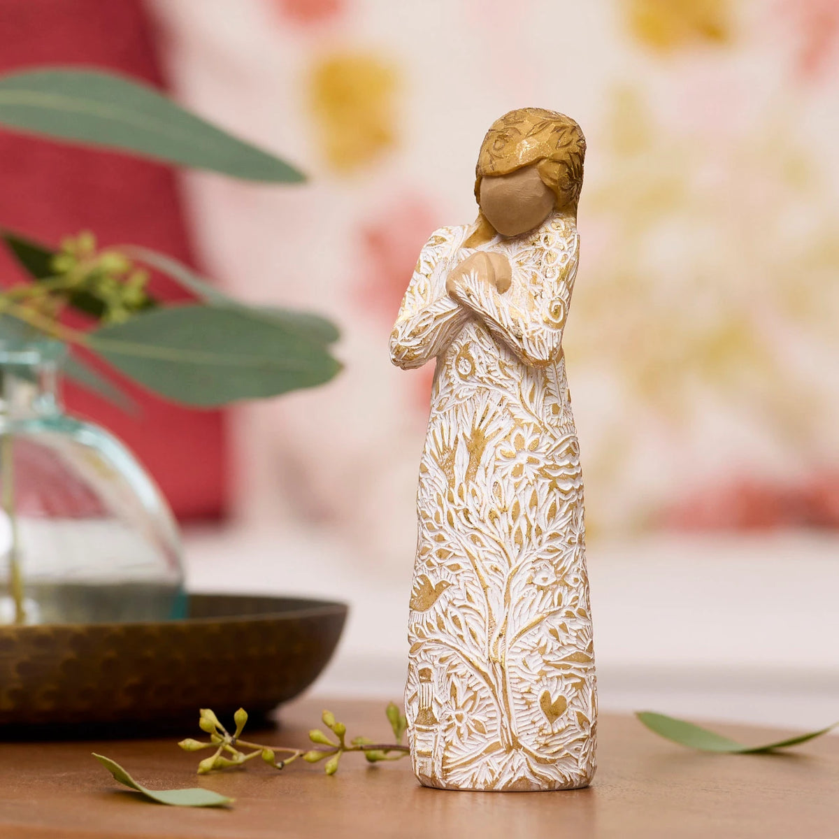 Willow Tree Tapestry, 5”h hand-painted standing resin figure, in cream dress, hands crossed at chest, entire figure carved with symbols of nature with gold-leaf, on table in warm light