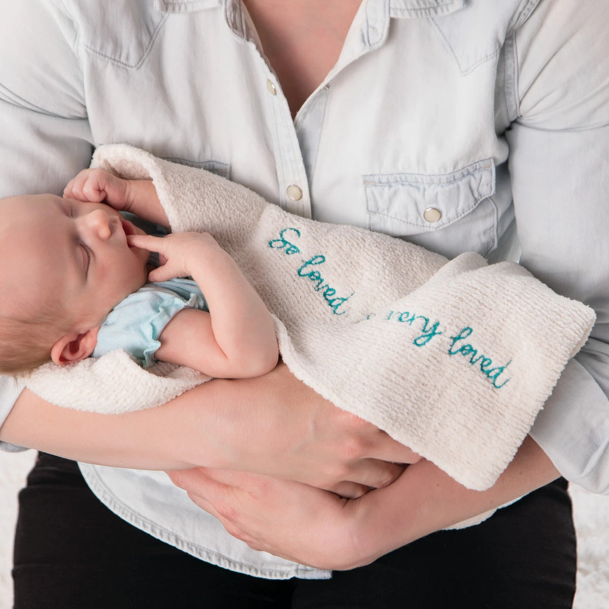 Close view of mother holding baby wrapped in cream towel that says 'so loved, so very loved' in blue