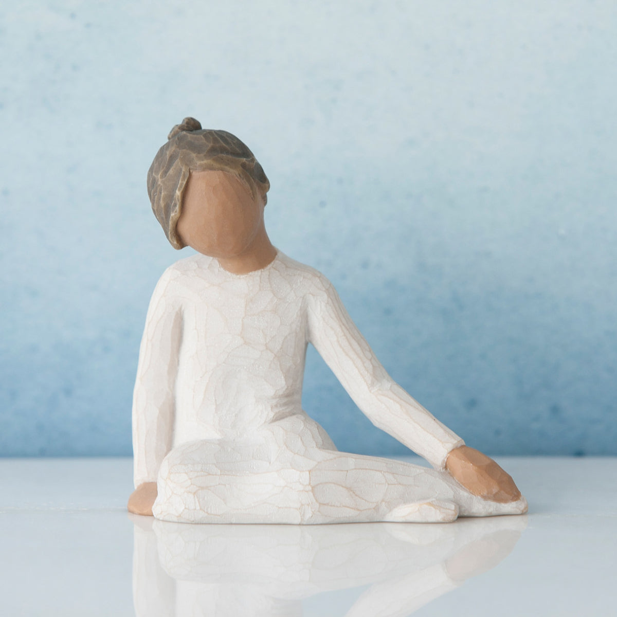 Faceless woman figurine in white dress sitting don on her knees - blue background