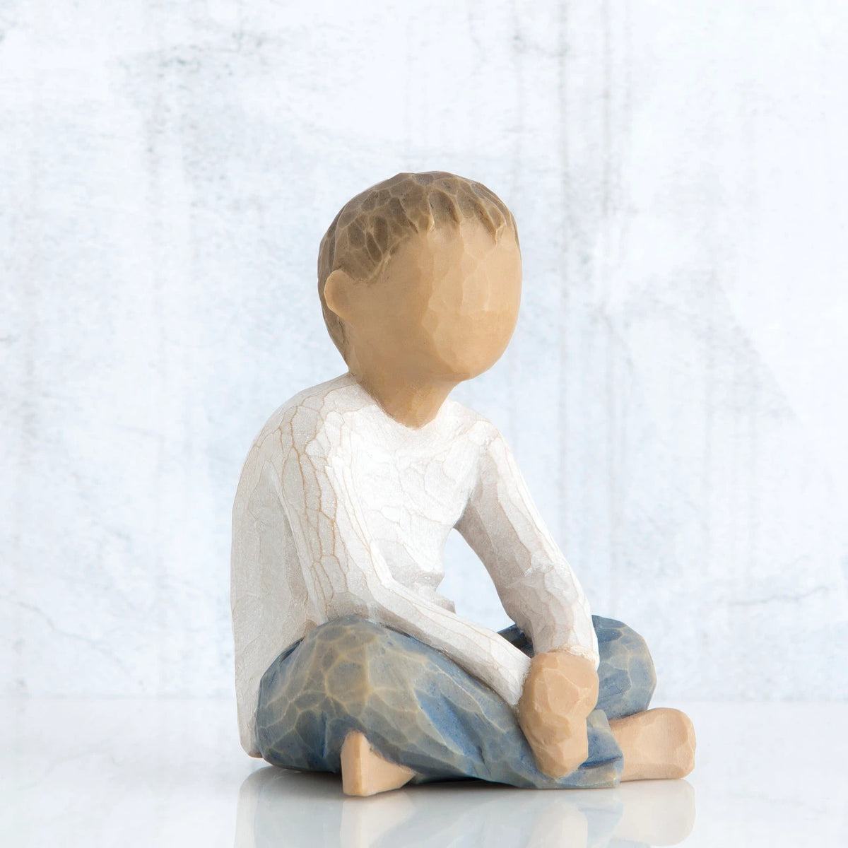 Small little boy figurine sitting down faceless, wearing white shirt and blue jeans