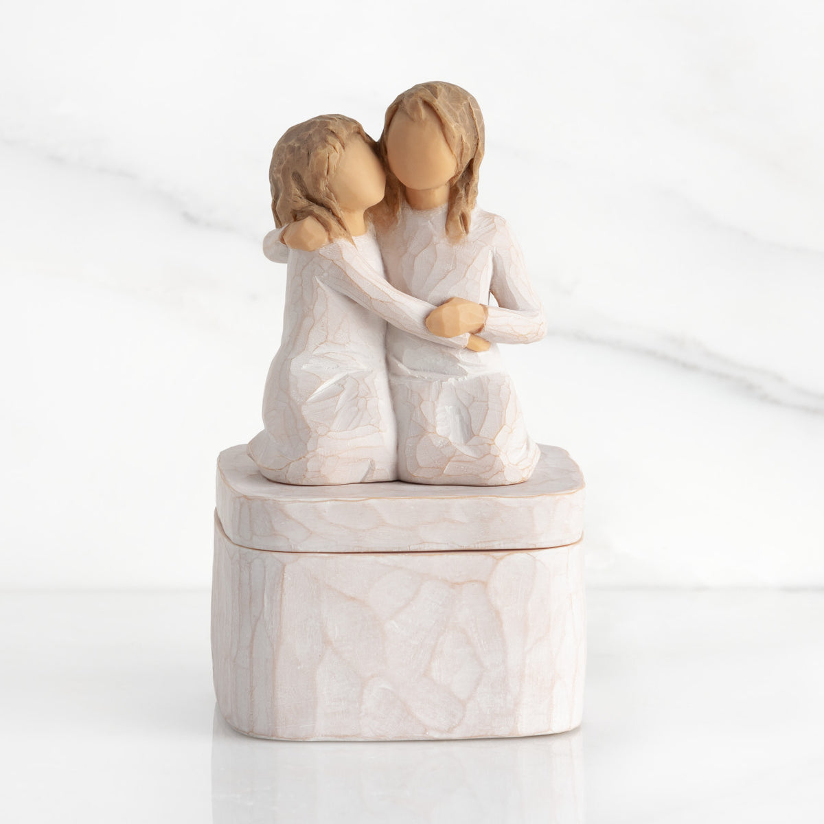 Square resin box, two 3-D figures kneeling atop lid, in cream dresses, hugging each other