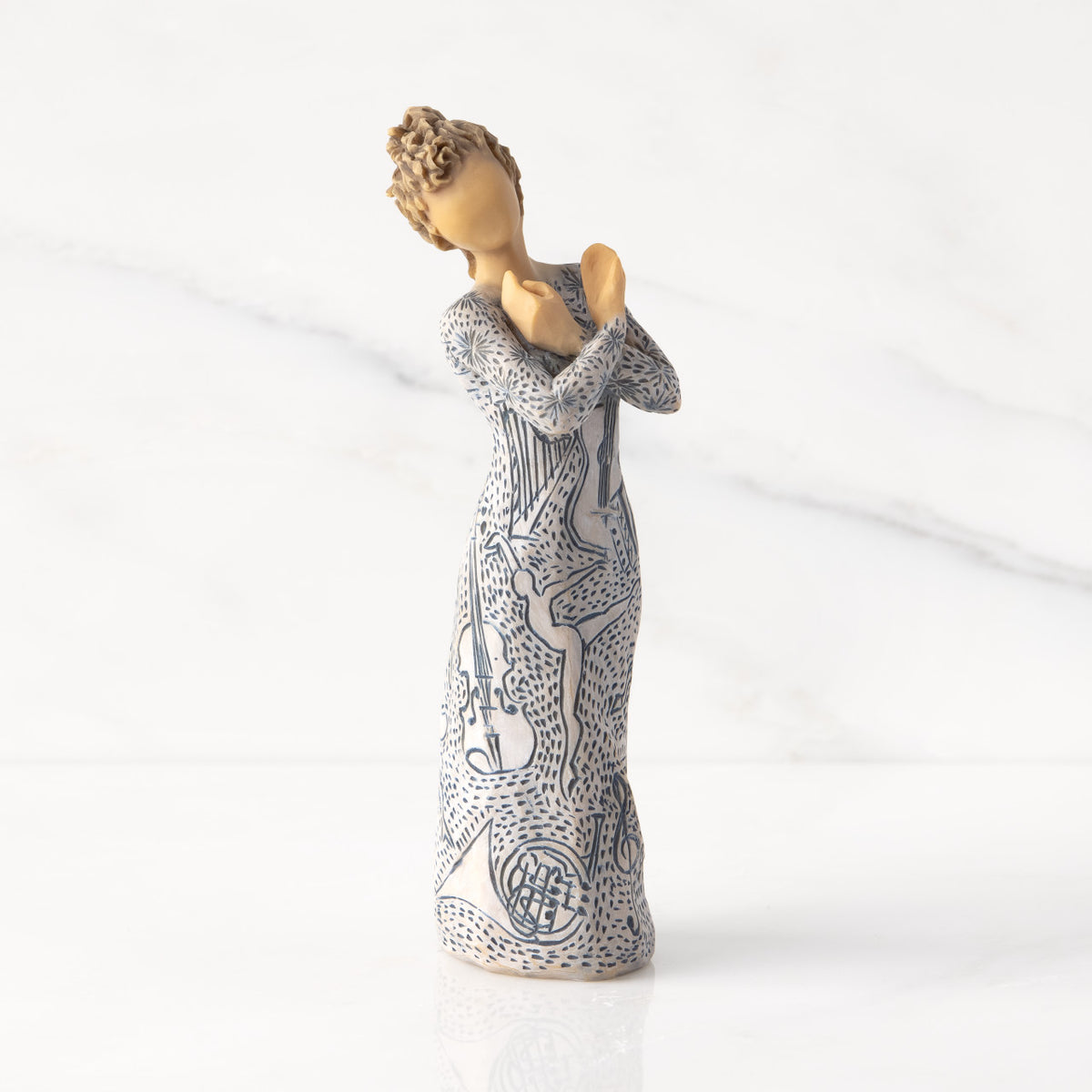 Front view: Lighter-skin figure carved with contrasting pattern of dark blue musical symbols, instruments, dancing forms