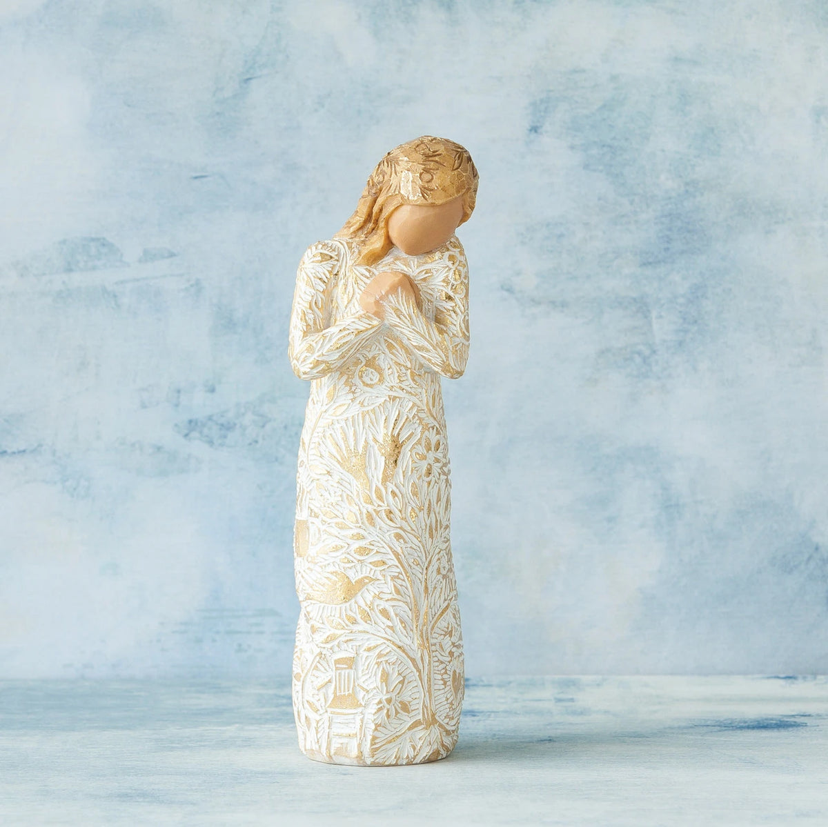 Willow Tree Tapestry, 5”h hand-painted standing resin figure, in cream dress, hands crossed at chest, entire figure carved with symbols of nature with gold-leaf, in front of blue painting