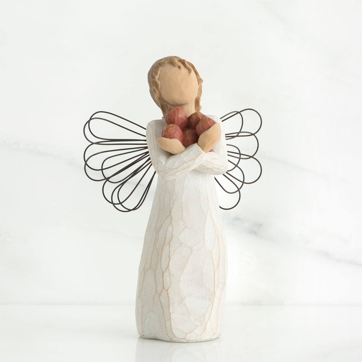 Young faceless girl figurine wearing white dress and black wire wings, holding red rocks in her hand