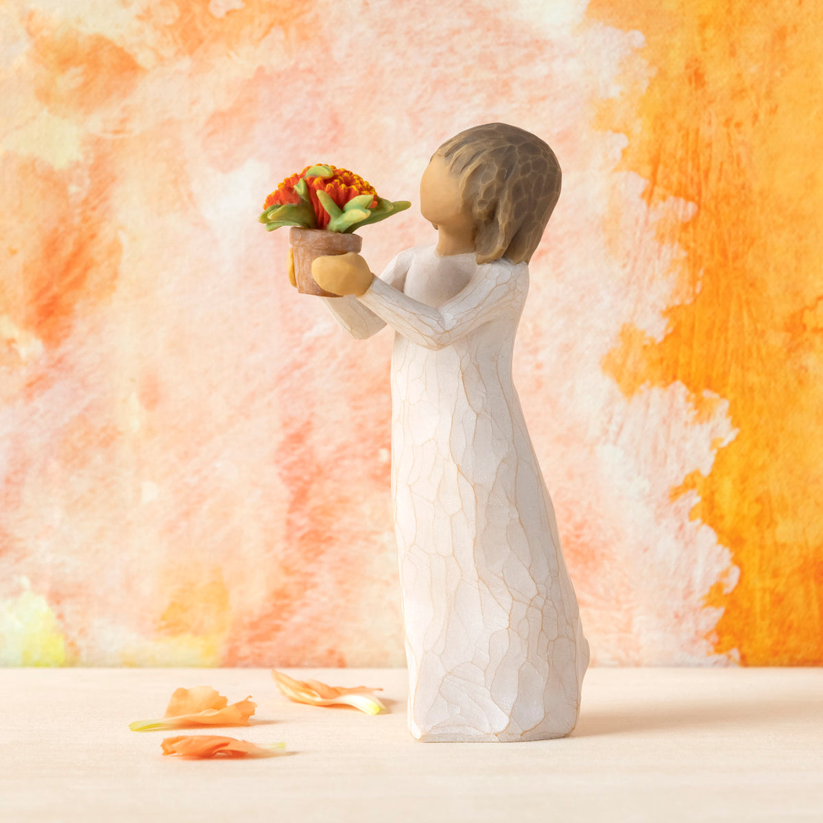 Willow Tree Little Things, 5.25”h hand-painted standing resin figure in cream dress, holding out terracotta pot with orange flowers, in front of orange painting