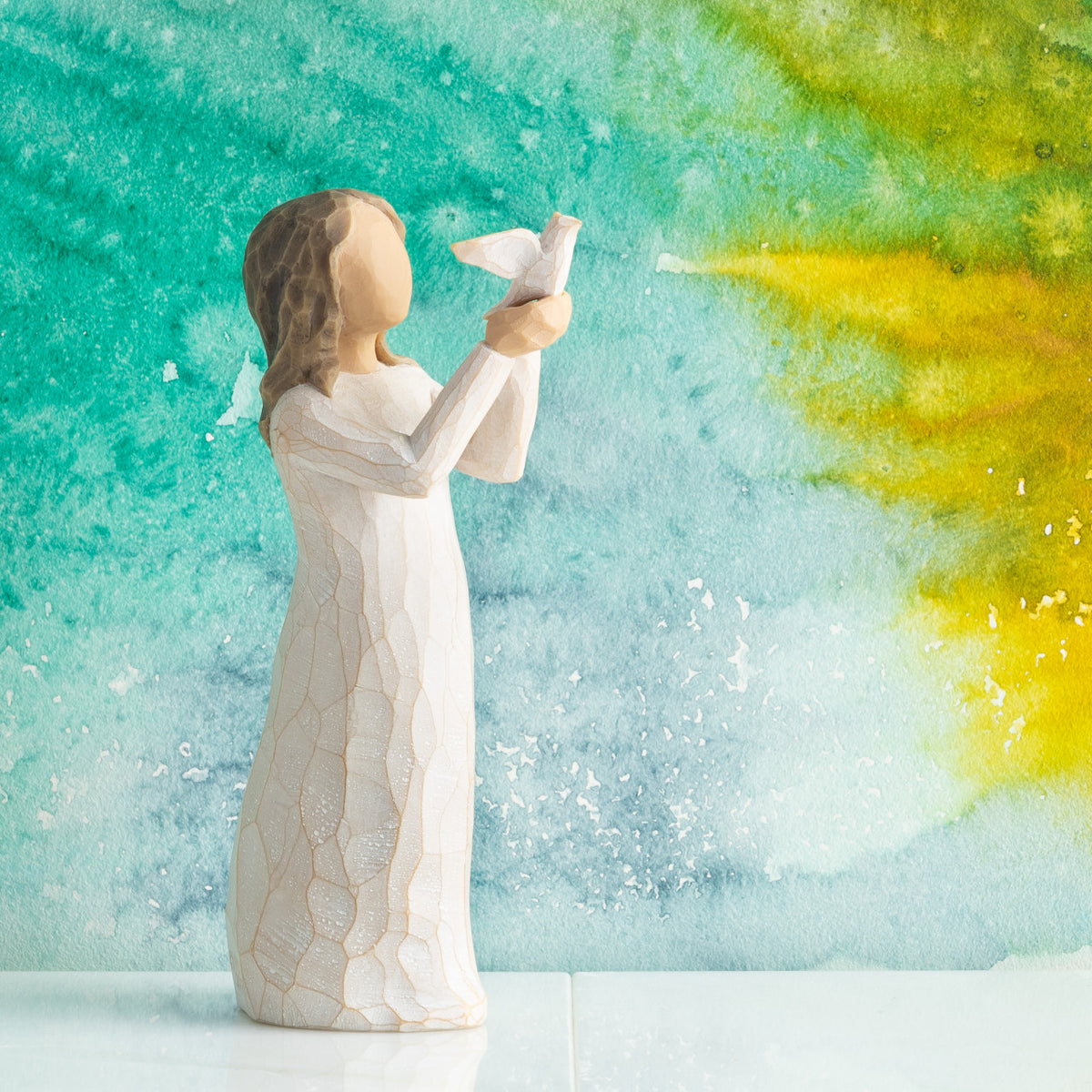 Willow Tree Soar, 5”h hand-painted standing figure in cream dress holding white dove in outstretched hands, in front of teal painting