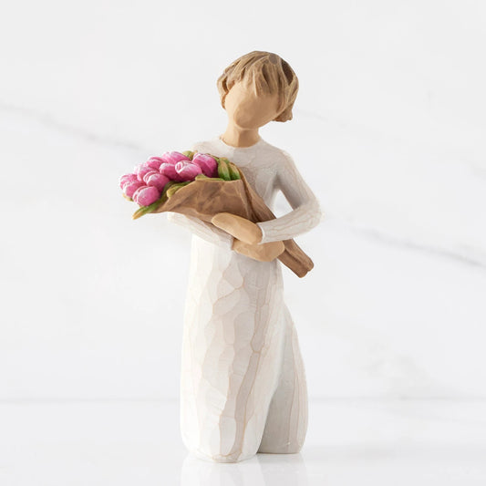 Front view of standing figure in cream dress holding bouquet of pink tulips