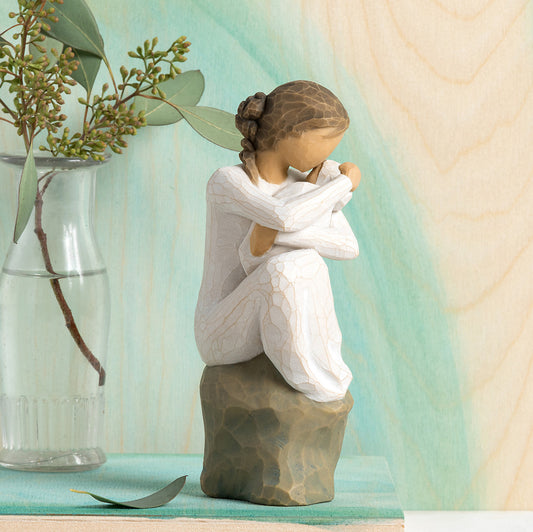 Willow Tree Guardian, 6”h hand-painted resin figure in cream dress, seated on gray rock, holding newborn baby in cream blanket, in front of celedon painting