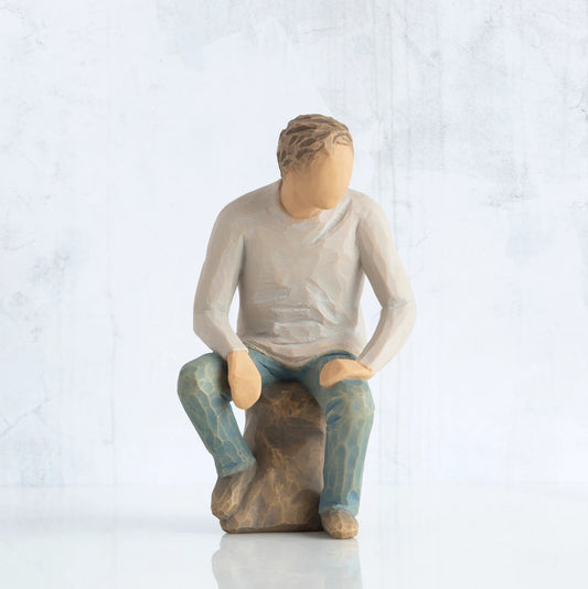 Front view, adult male figure in light gray shirt and blue jeans, seated on gray rock