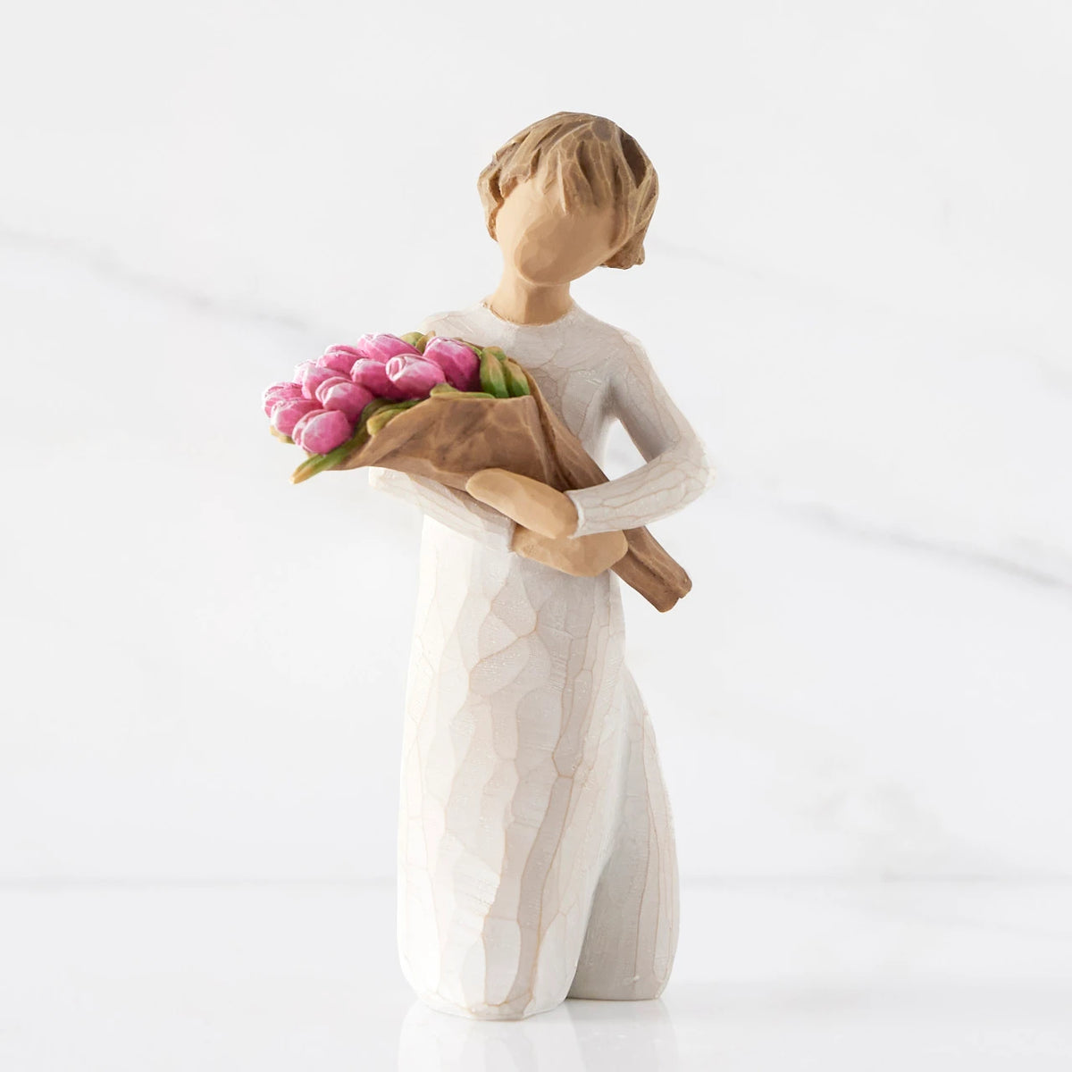 Front view of standing figure in cream dress holding bouquet of pink tulips