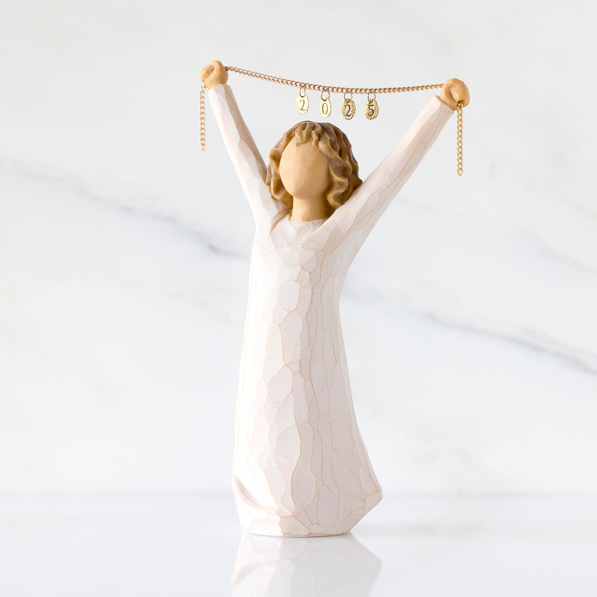 Front view: figure in cream dress holding gold chain above her head with year 2025 on it