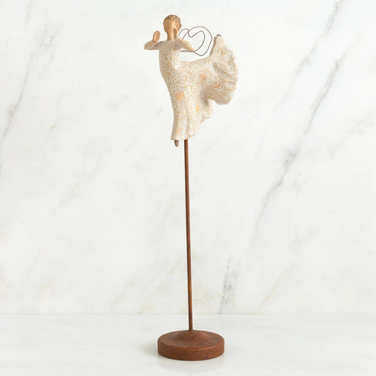 Far shot of angel figurine dressed in white dress dancing with arms and legs out - she is on a brown wooden stand