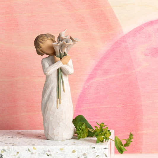 Willow Tree Beautiful Wishes, 5.5”h hand-painted standing resin figure in cream dress, holding bouquet of white calla lilies, in front of pink painting