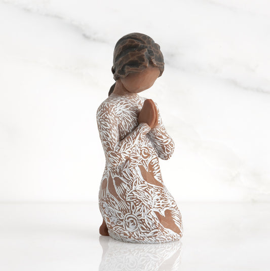 Front: Kneeling figure with darker skin, hands in position of prayer or meditation in cream dress carved with icons of nature