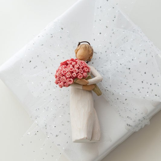 Willow Tree Abundance Ornament, 4”h hand-painted resin figure in cream dress, holding bouquet of pink roses, brown elastic cord, tied to wrapped gift