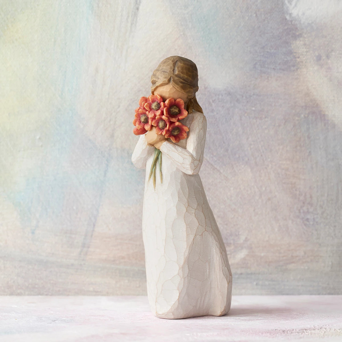 Willow Tree Surrounded by Love, 5"h hand-painted standing resin figure in cream dress, holding large bouquet of red-orange poppies up to face, in front of pastel painting