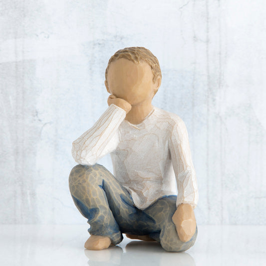 Small faceless boy figurine sitting with elbow on knee - wearing white shirt and blue jeans