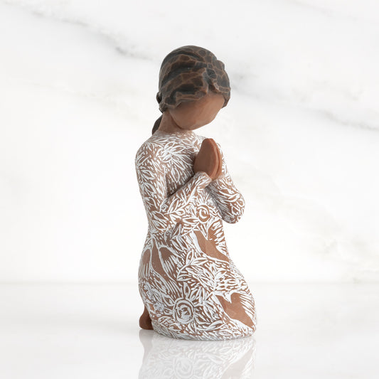 Front: Kneeling figure with darker skin, hands in position of prayer or meditation in cream dress carved with icons of nature