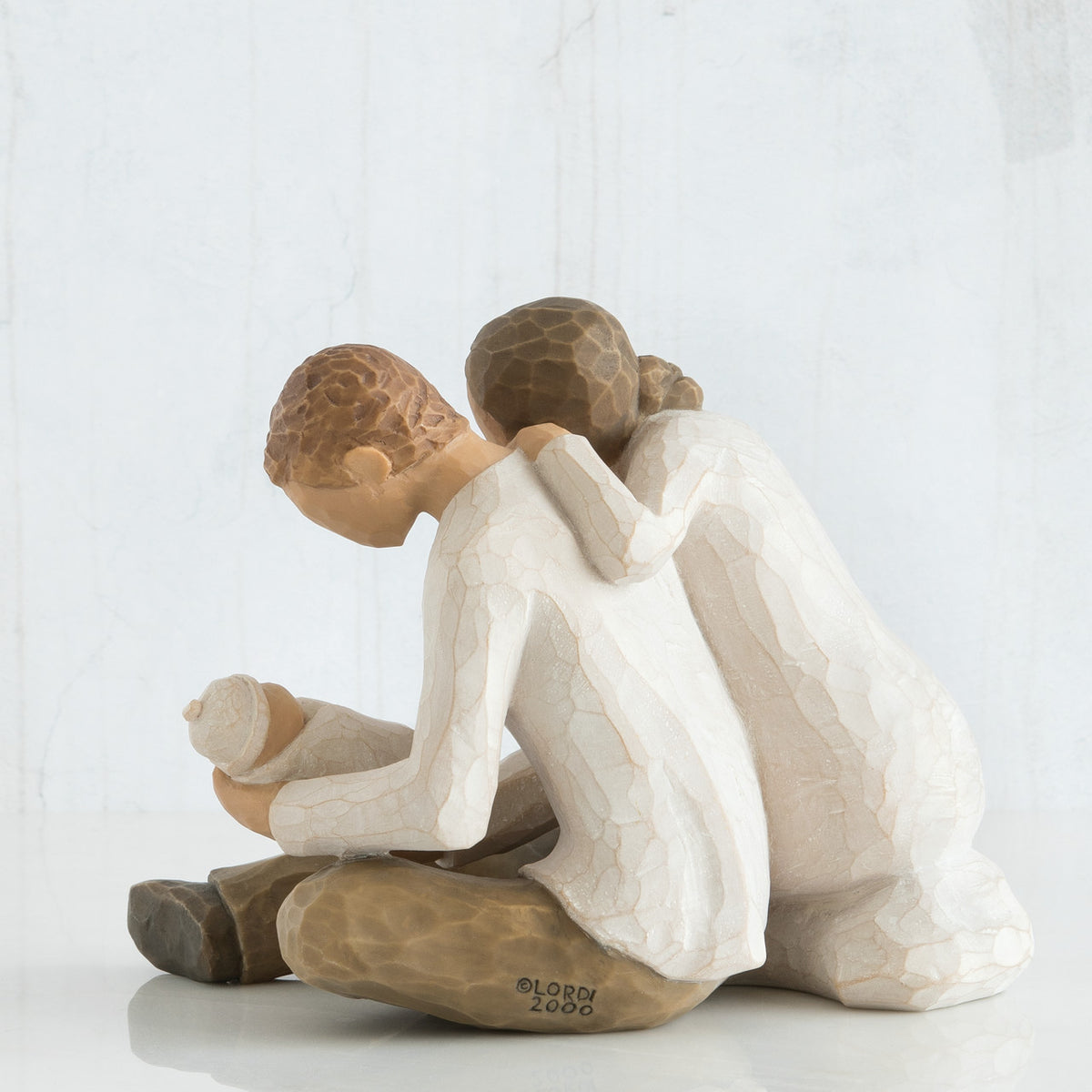 Man and woman couple figurines in white sitting down holding swaddled baby