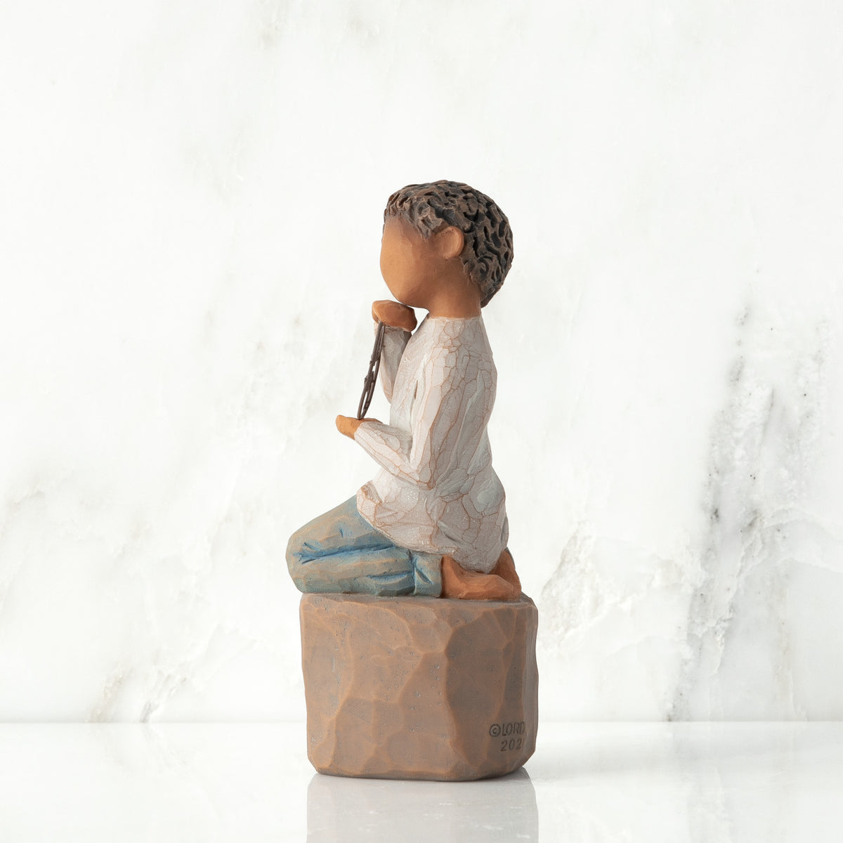 Left view: Figure of darker-skin child, kneeling on rock, holding wire circle with ‘love you’ written in wire