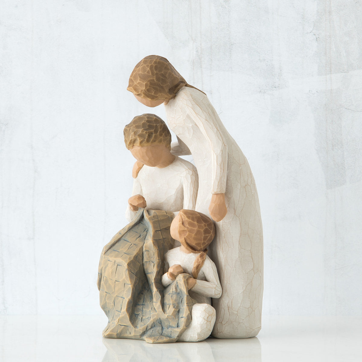 Man and woman figurines sitting down with blanket next to young girl figurine