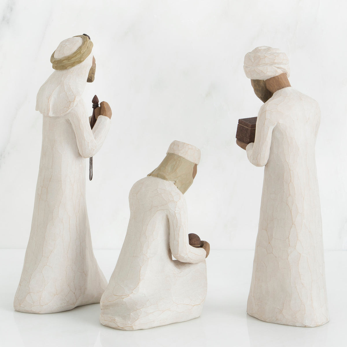 Set of three wiseman figurines in white standing facing the back holding boxes