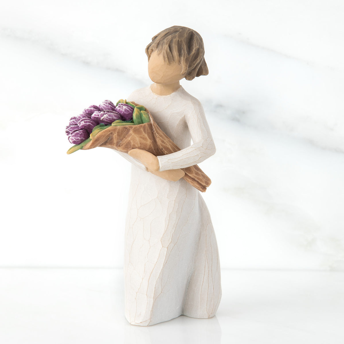 Standing figure with short brown hair wearing long cream dress holding large bouquet of purple tulips, facing left