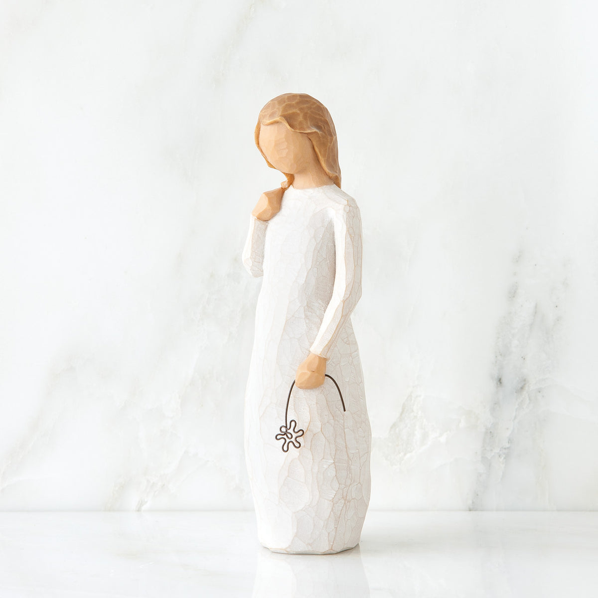 Front view of blonde girl figurine in white dress standing holding black flower