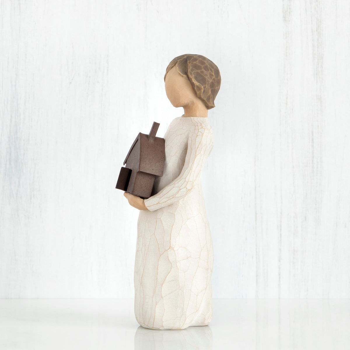 Side view of brunette figurine in white dress holding brown house figurine