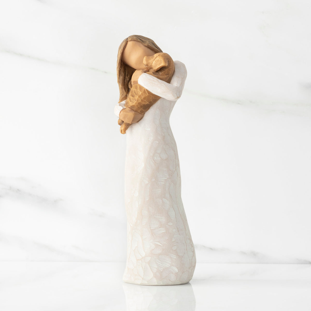 Left view, standing female figure in cream dress, holding golden color puppy in her arms