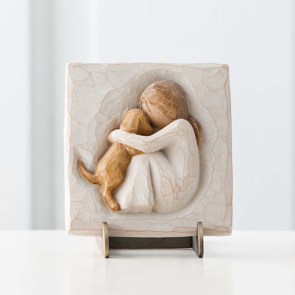 Close view of small cream square plaque on stand with carved in image of girl figurine hugging golden puppy