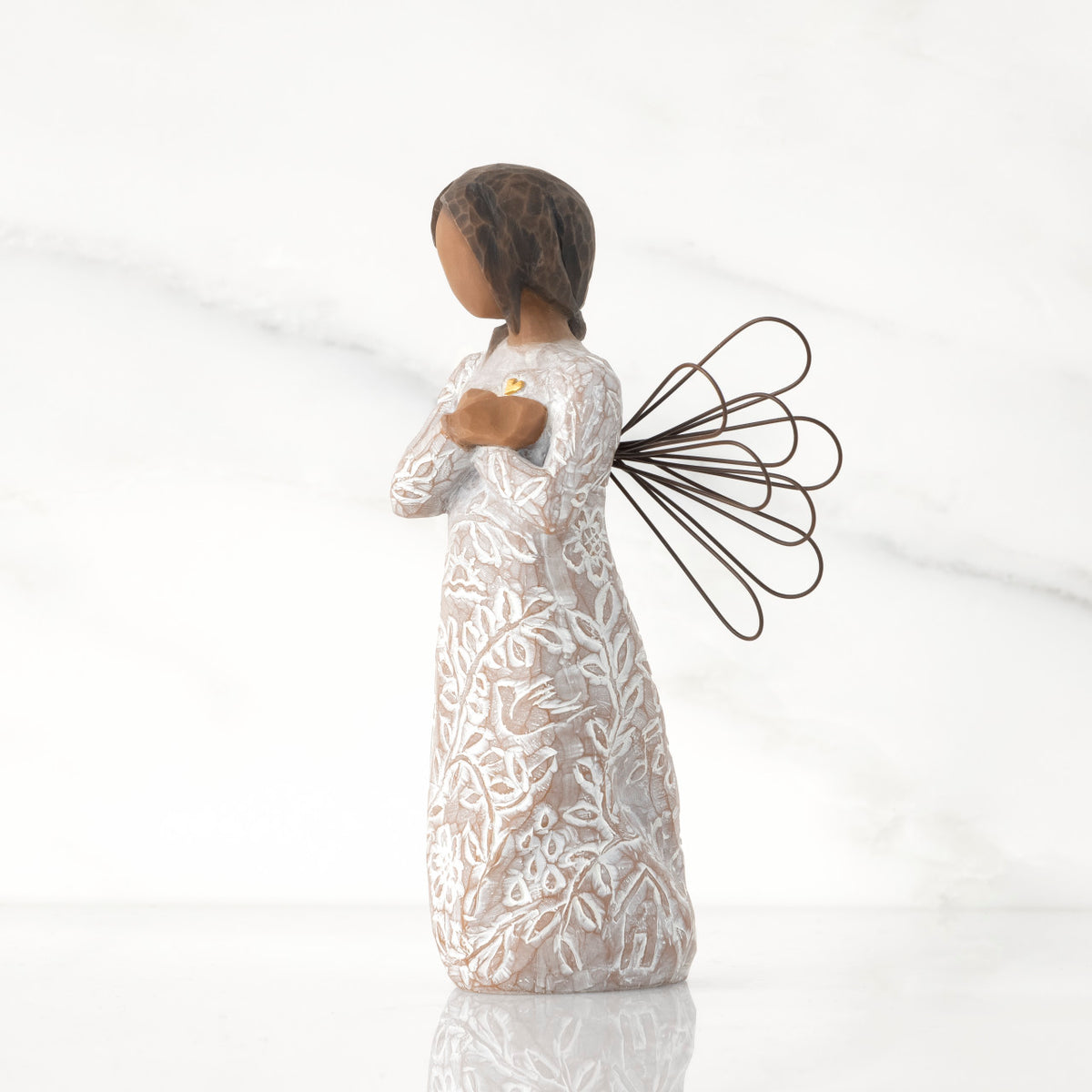 Facing left: angel with wire wings, darker skin, arms crossed over gold heart, dress carved with symbols of remembrance