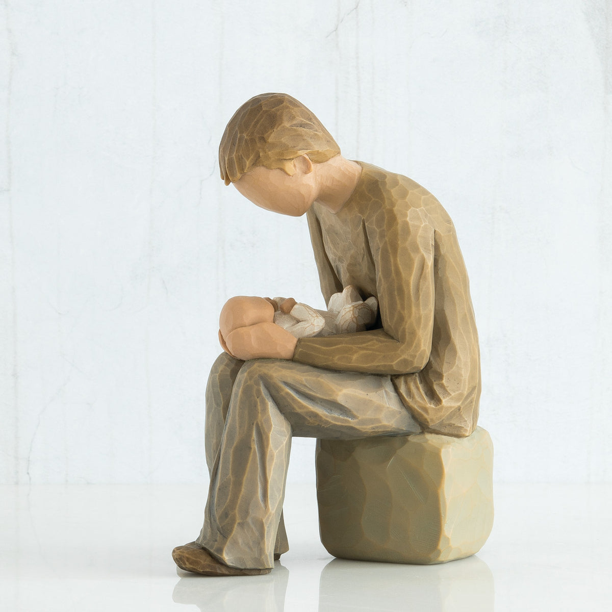 Side view of man figurine dressed in brown sitting on a rock holding baby figurine