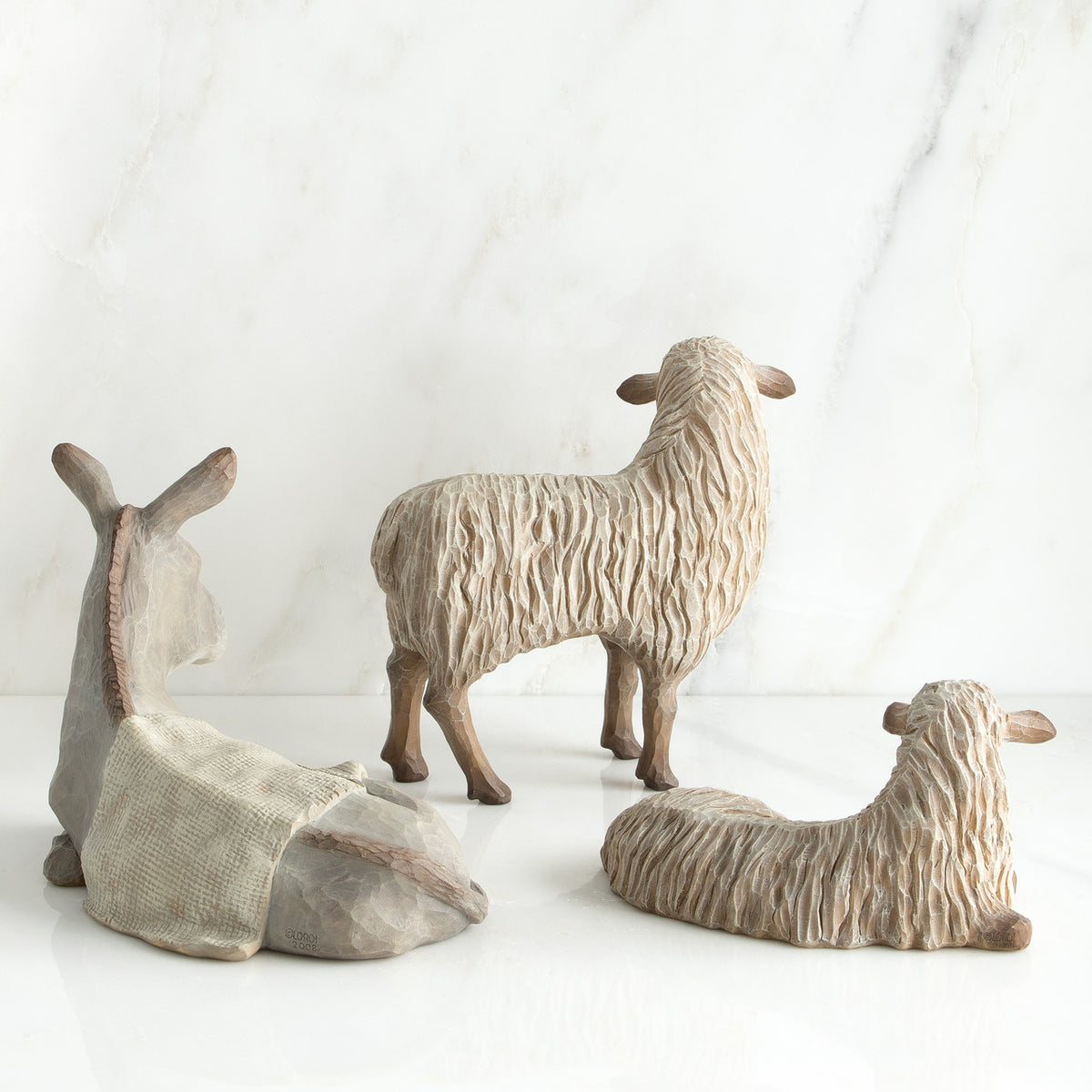 White donkey figurine laying down next to two white sheep figurines