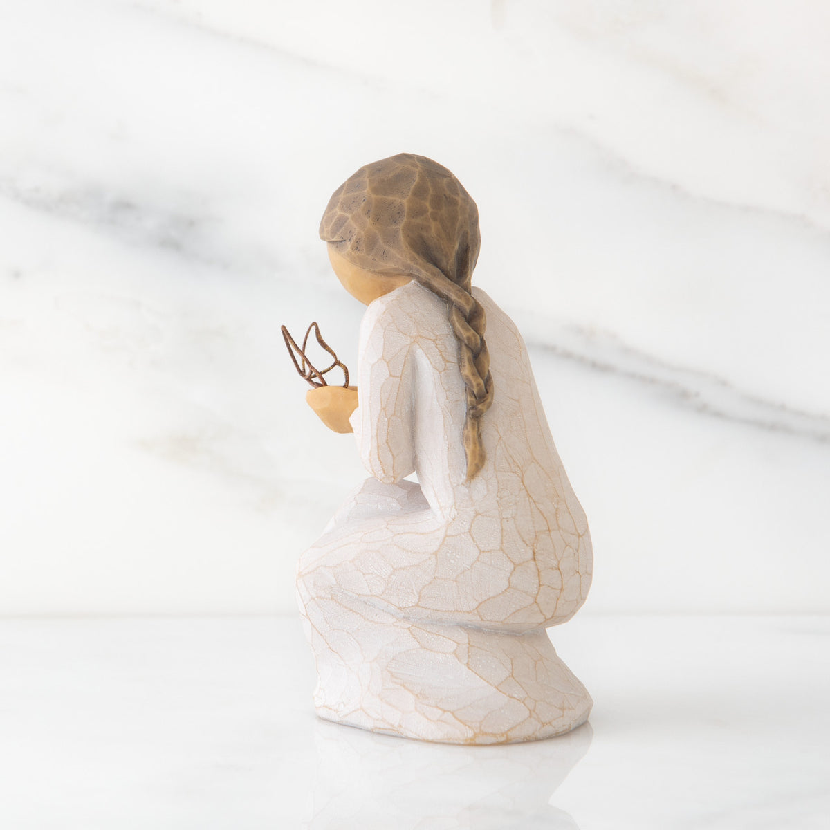 Left back view of kneeling female figure in cream dress, with wire butterfly on extended hands