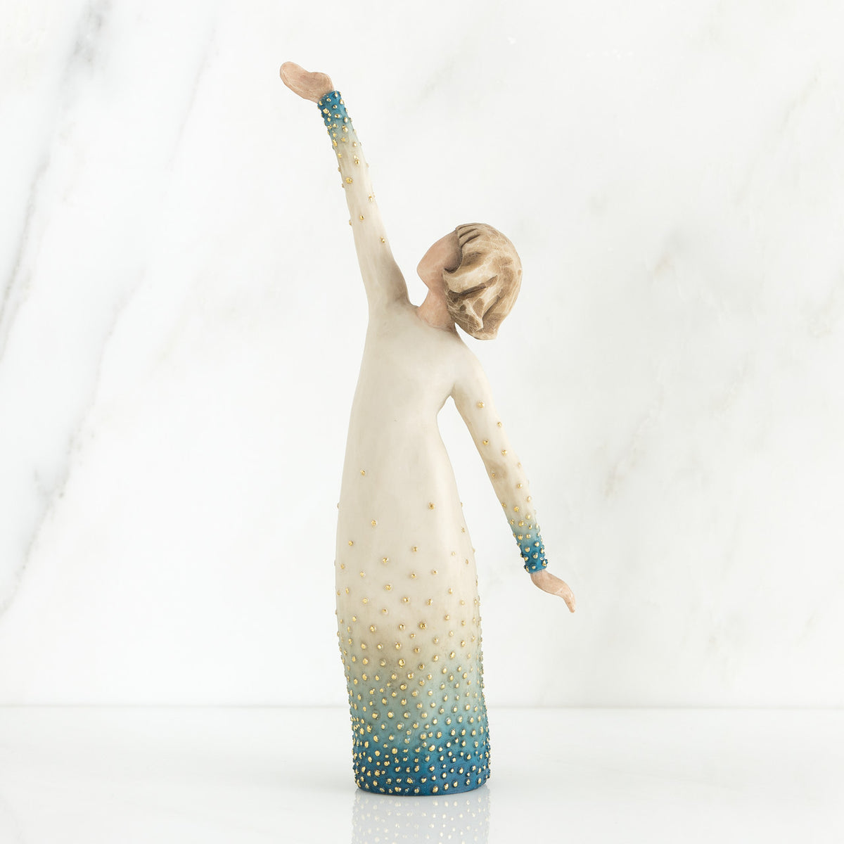 Faceless woman figurine in white dress with blue embellishments - she is facing away from the camera holding both her arms in opposite directions