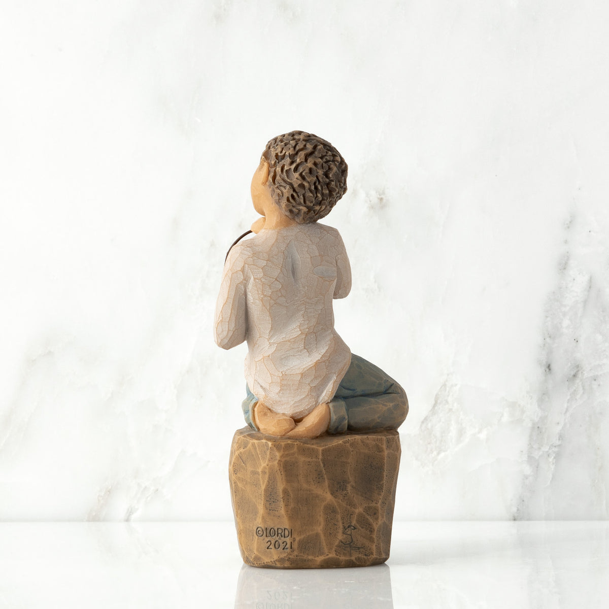 Back view: Figure of lighter-skin child, kneeling on rock, holding wire circle with ‘love you’ written in wire