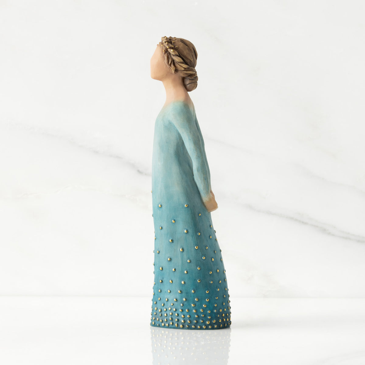 Facing left profile: Lighter-skin figure, arms clasped behind back, hair and deep blue ombré garment dotted with gold leaf