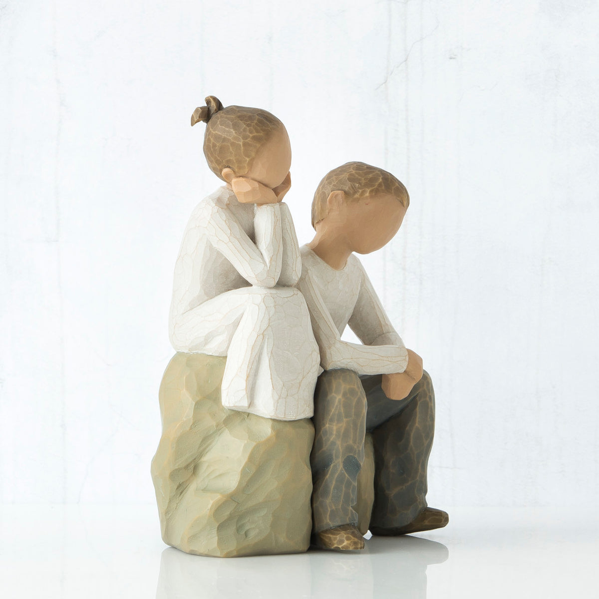 Small young girl figurine in white next to small young boy figurine - sitting on rock