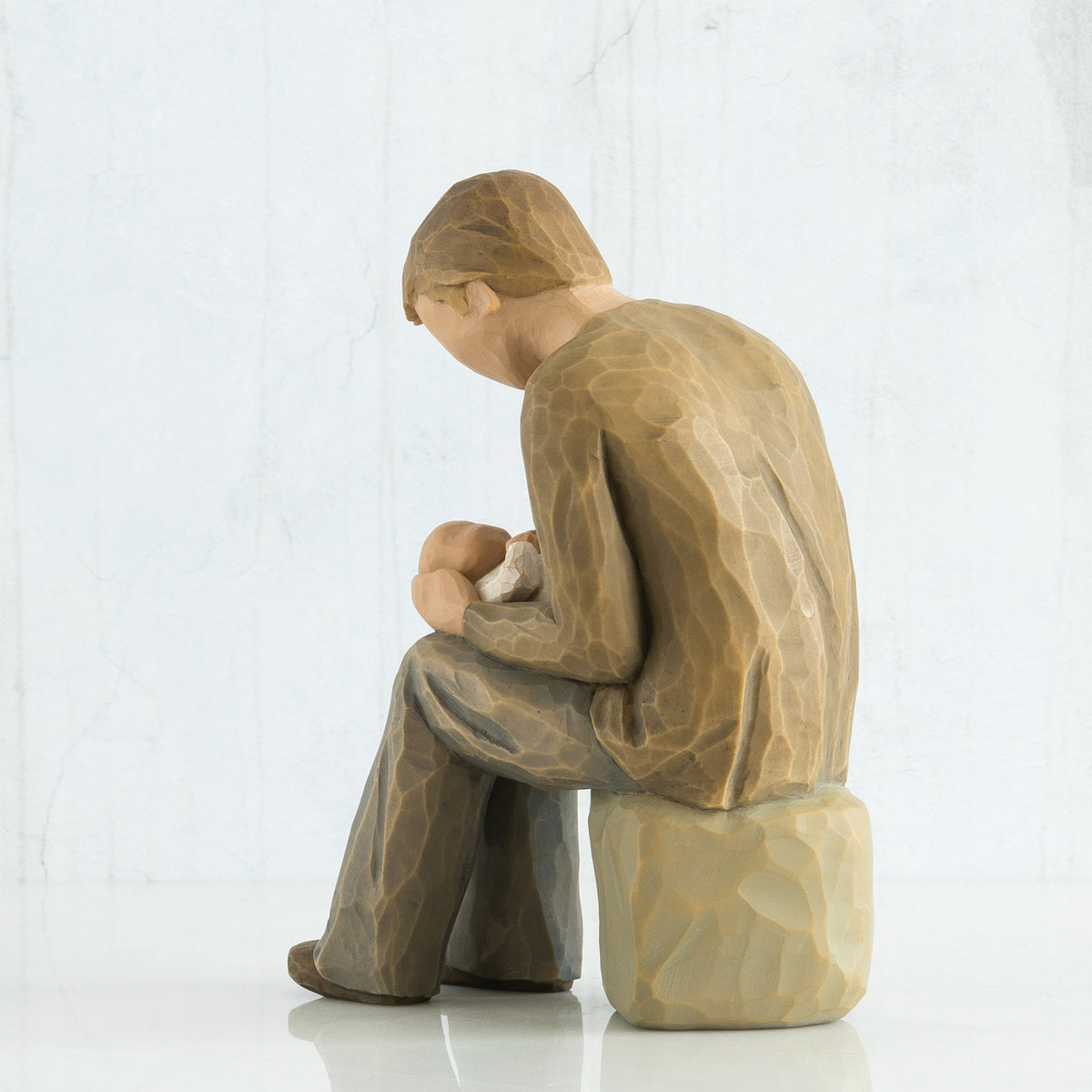 Back view of man figurine in brown clothes sitting on rock holding baby