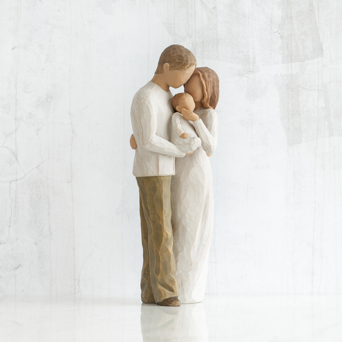 Man and woman figurines in white facing one another holding baby