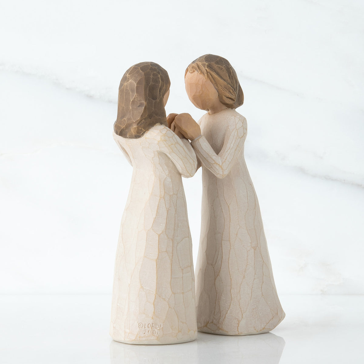 Close view of two brunette figurines in white dresses facing one another holding hands