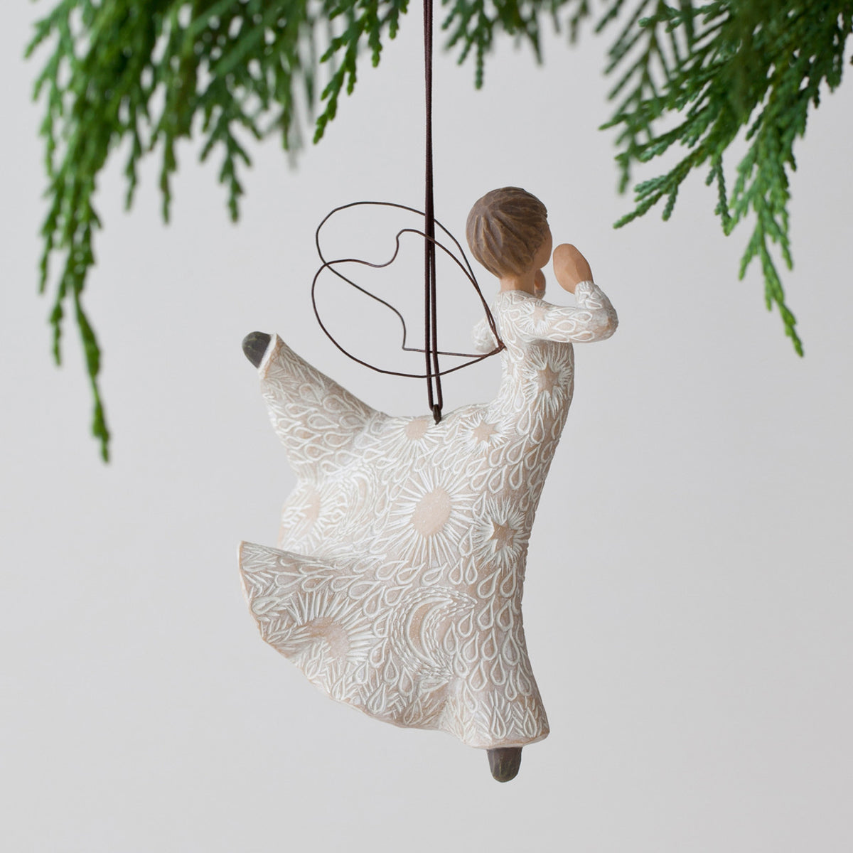 Side view of angel figurine ornament hanging from green christmas tree