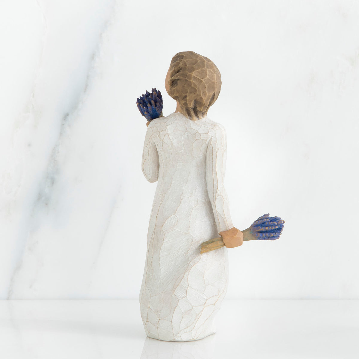 Back view of brunette girl figurine in white dress holding blue flowers