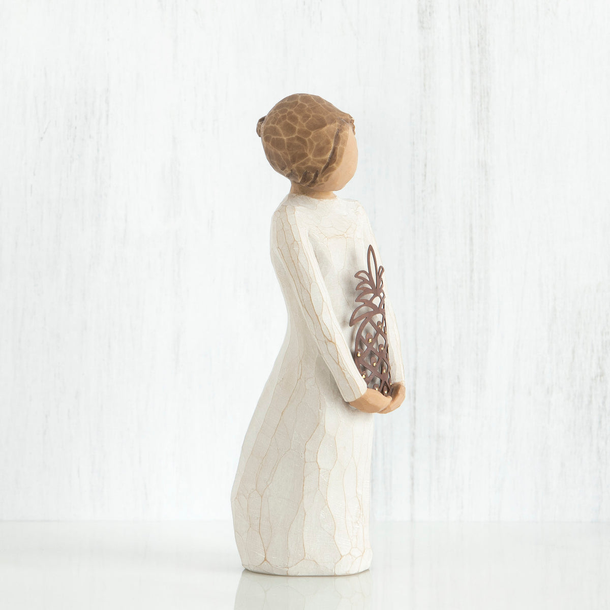 Left side view of girl with brown hair in a bun holding a pineapple with both hands