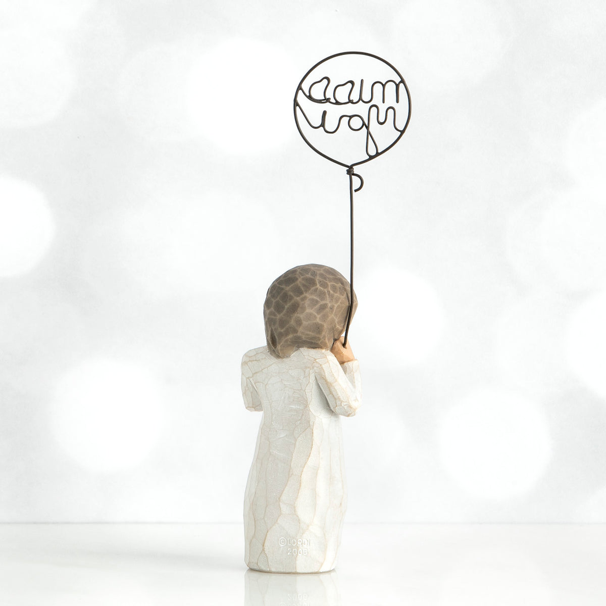 Back view of brunette small girl figurine in white dress holding up black wire balloon