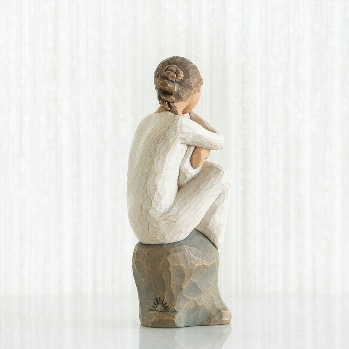 Back view of brunette girl figurine sitting down in white dress on rock