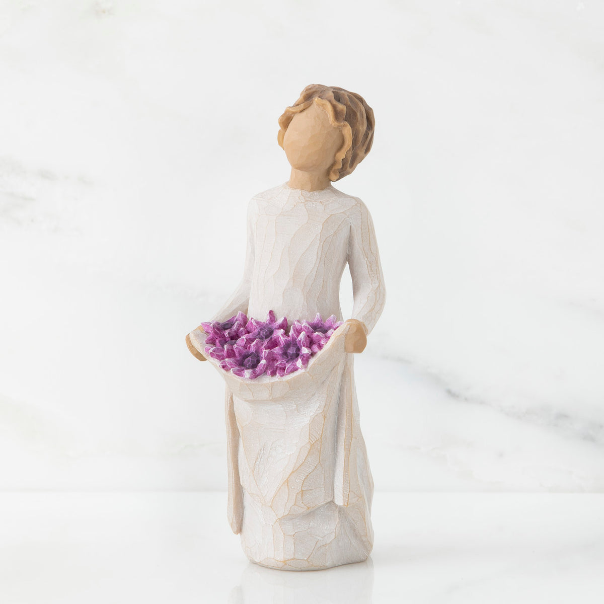 Front view of woman with tied back, curly, light brown hair holds up a portion of her dress's skirt as it is full of purple flowers